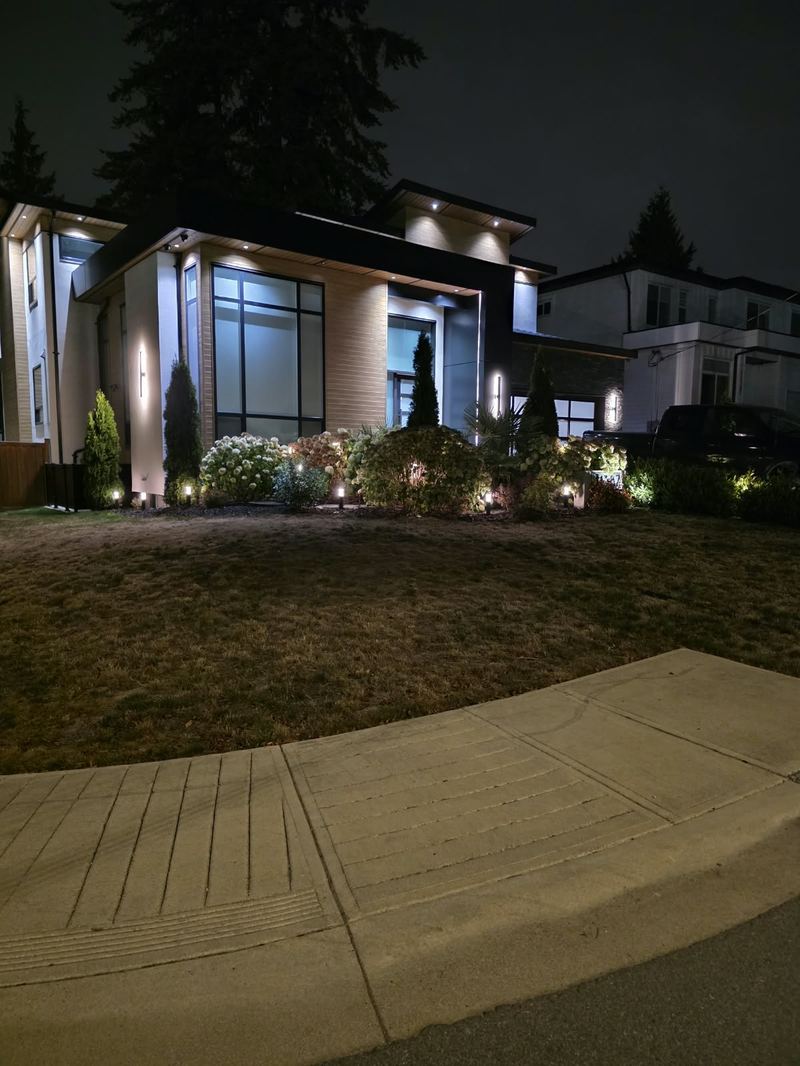Modern two-storey home in Delta, BC with facade up-lighting and lit foundation planting at night